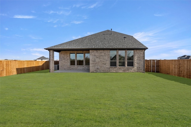 rear view of property with a fenced backyard, a shingled roof, a yard, and brick siding