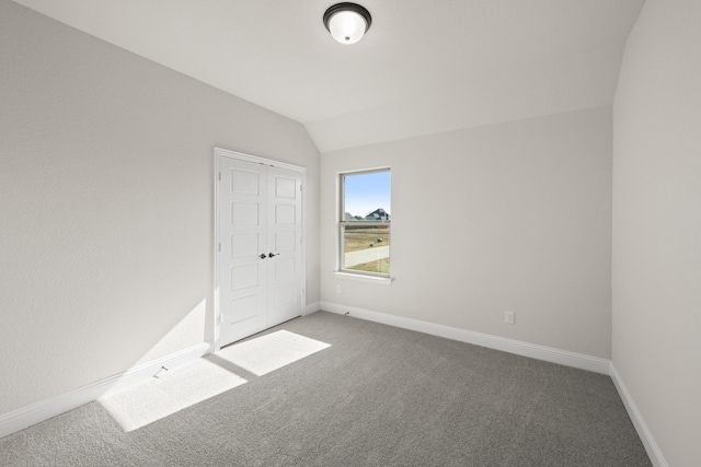 unfurnished bedroom with carpet floors, baseboards, lofted ceiling, and a closet
