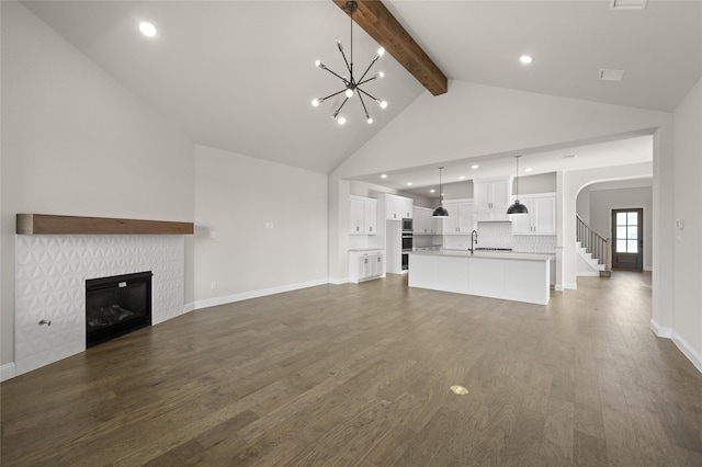 unfurnished living room featuring a sink, high vaulted ceiling, beamed ceiling, a chandelier, and a glass covered fireplace