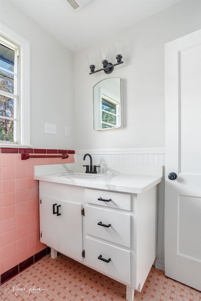 bathroom with plenty of natural light, wainscoting, vanity, and tile walls