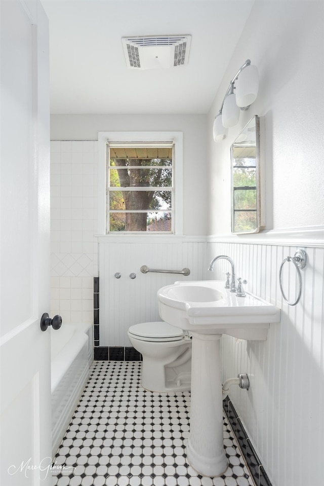 bathroom featuring visible vents, toilet, a wainscoted wall, a tub, and walk in shower