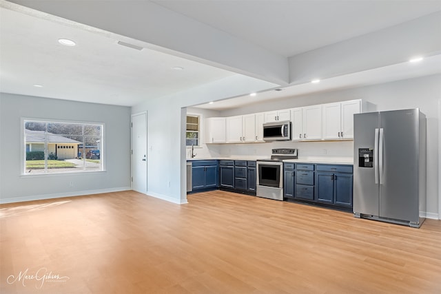 kitchen with blue cabinetry, tasteful backsplash, light hardwood / wood-style floors, white cabinets, and appliances with stainless steel finishes