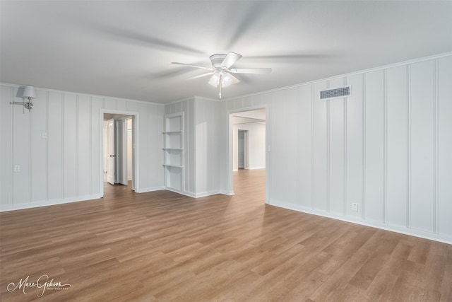 unfurnished room with crown molding, visible vents, a decorative wall, light wood-style floors, and ceiling fan