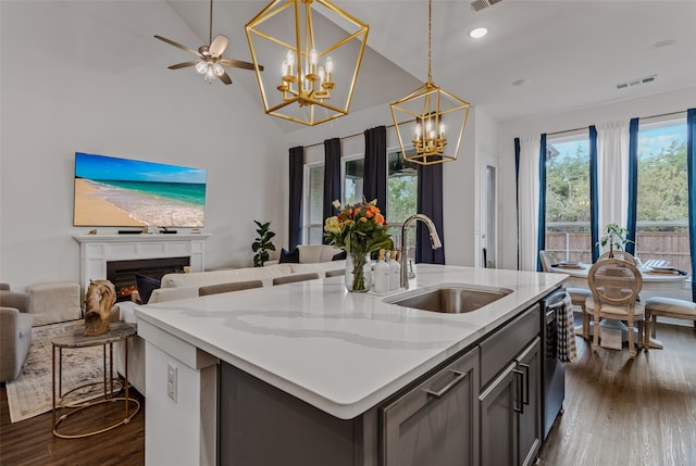 kitchen featuring sink, dark hardwood / wood-style flooring, hanging light fixtures, light stone counters, and a center island with sink