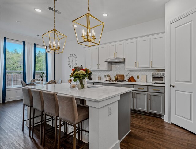 kitchen featuring dark wood-type flooring, a kitchen island with sink, a kitchen breakfast bar, and hanging light fixtures