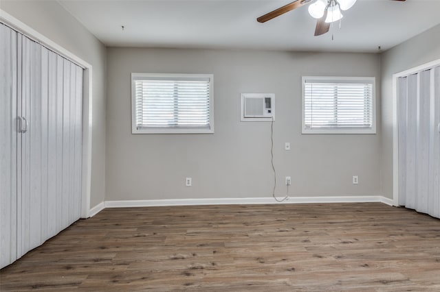 unfurnished bedroom featuring multiple windows, ceiling fan, a wall mounted air conditioner, and hardwood / wood-style flooring