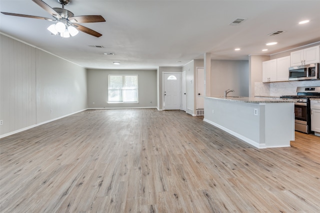 kitchen with white cabinets, stainless steel appliances, light hardwood / wood-style flooring, and a kitchen island with sink