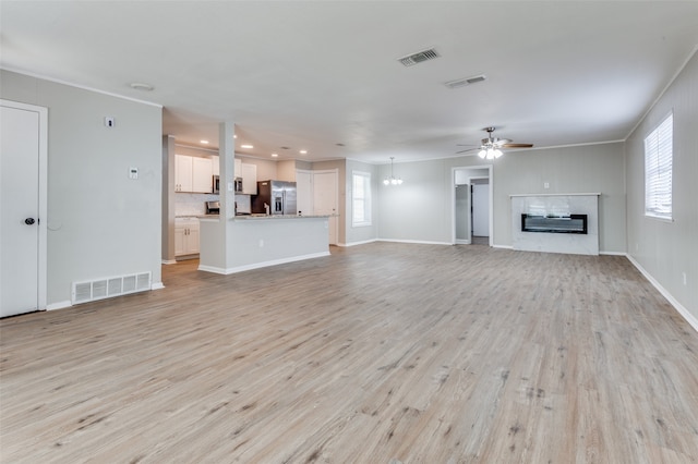 unfurnished living room featuring a wealth of natural light, light hardwood / wood-style flooring, crown molding, and ceiling fan with notable chandelier