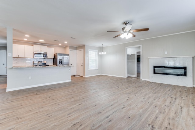 unfurnished living room with crown molding, a high end fireplace, ceiling fan with notable chandelier, and light hardwood / wood-style floors