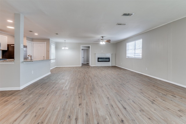 unfurnished living room with ceiling fan with notable chandelier, light wood-type flooring, and ornamental molding