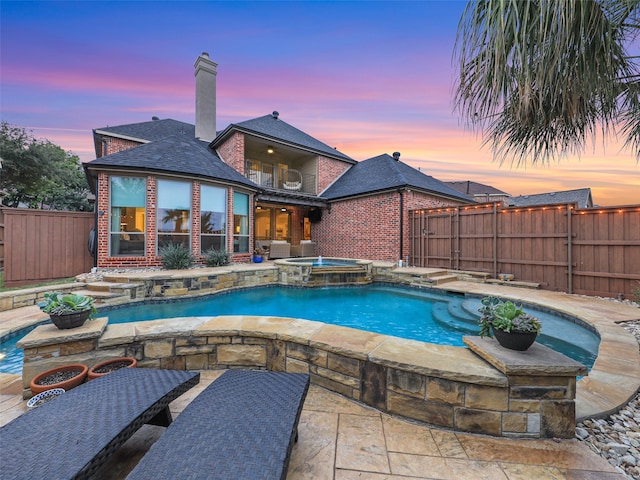 pool at dusk with an in ground hot tub and a patio area