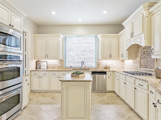 kitchen featuring light stone countertops, stainless steel appliances, cream cabinetry, and sink