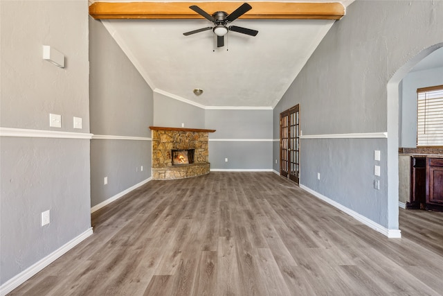 unfurnished living room featuring ceiling fan, vaulted ceiling with beams, light hardwood / wood-style flooring, a fireplace, and crown molding