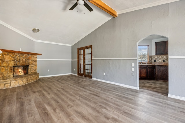 unfurnished living room with a stone fireplace, wood-type flooring, ornamental molding, and vaulted ceiling with beams