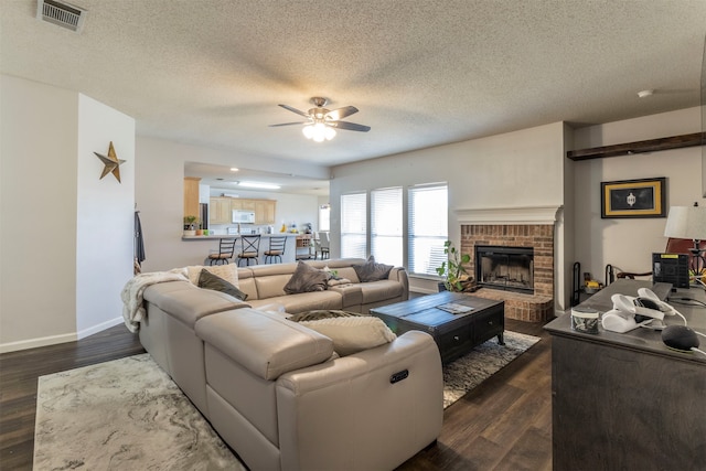 living room featuring a brick fireplace, a textured ceiling, dark hardwood / wood-style floors, and ceiling fan