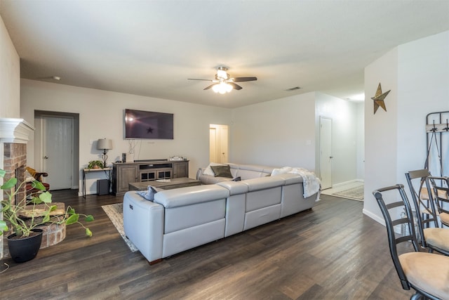 living room with dark wood-type flooring, ceiling fan, and a brick fireplace