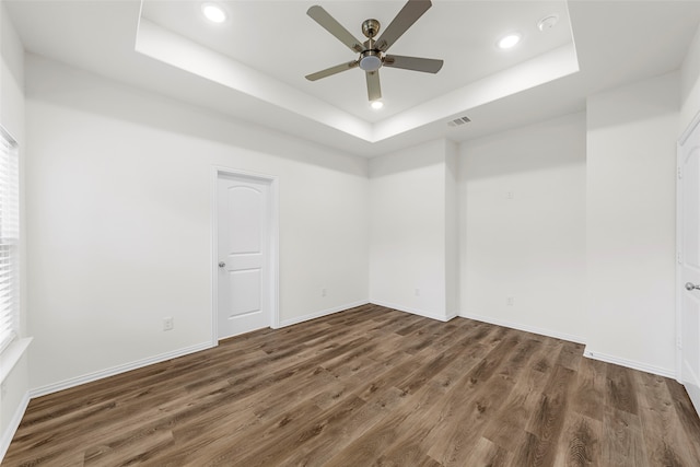 empty room with ceiling fan, a raised ceiling, and dark hardwood / wood-style flooring