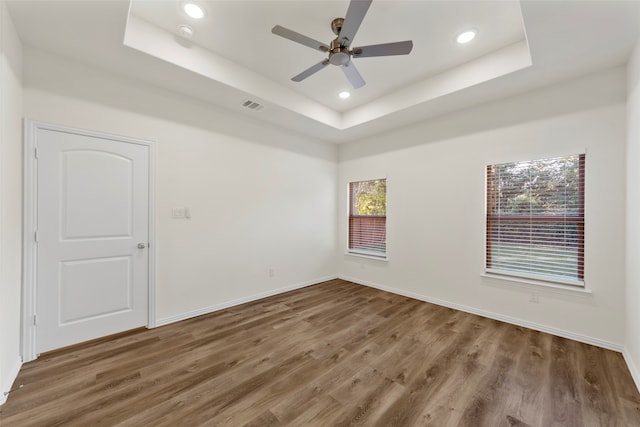 empty room featuring ceiling fan, hardwood / wood-style flooring, a tray ceiling, and plenty of natural light