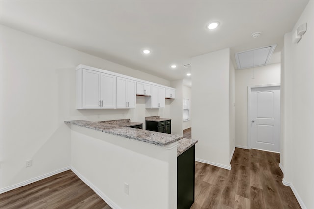 kitchen with kitchen peninsula, white cabinets, light stone countertops, and wood-type flooring