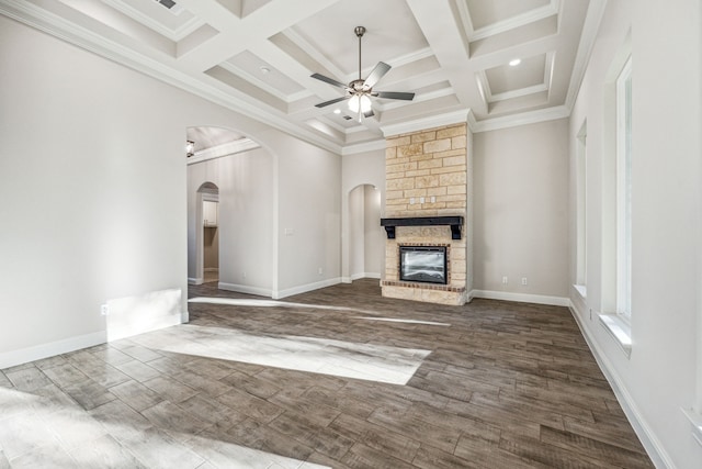 unfurnished living room with coffered ceiling, ceiling fan, crown molding, hardwood / wood-style floors, and a stone fireplace