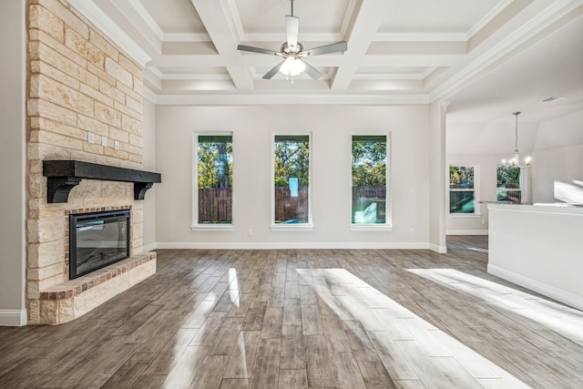 unfurnished living room with coffered ceiling, a stone fireplace, hardwood / wood-style floors, ceiling fan with notable chandelier, and ornamental molding