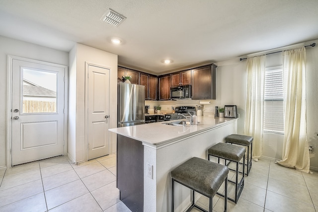 kitchen featuring sink, kitchen peninsula, a breakfast bar, light tile patterned floors, and black appliances