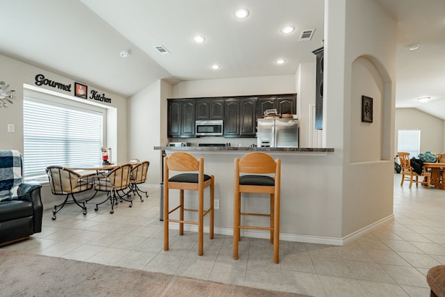 kitchen featuring kitchen peninsula, light tile patterned floors, a breakfast bar, vaulted ceiling, and stainless steel appliances