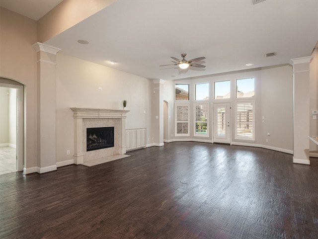 unfurnished living room with ceiling fan, a fireplace, ornate columns, and dark wood-type flooring