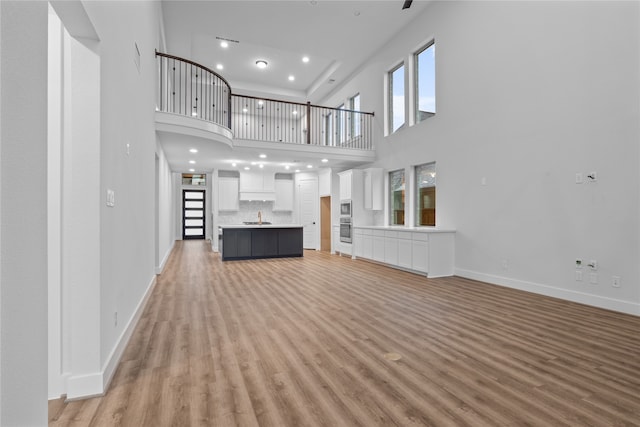 unfurnished living room featuring sink, light hardwood / wood-style flooring, and a towering ceiling