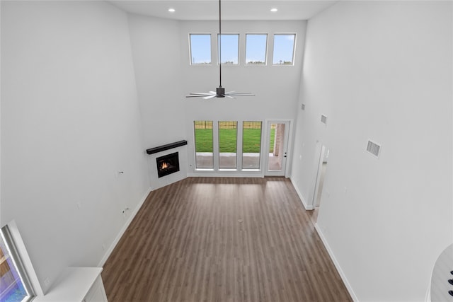 unfurnished living room featuring a high ceiling, dark hardwood / wood-style floors, a healthy amount of sunlight, and ceiling fan