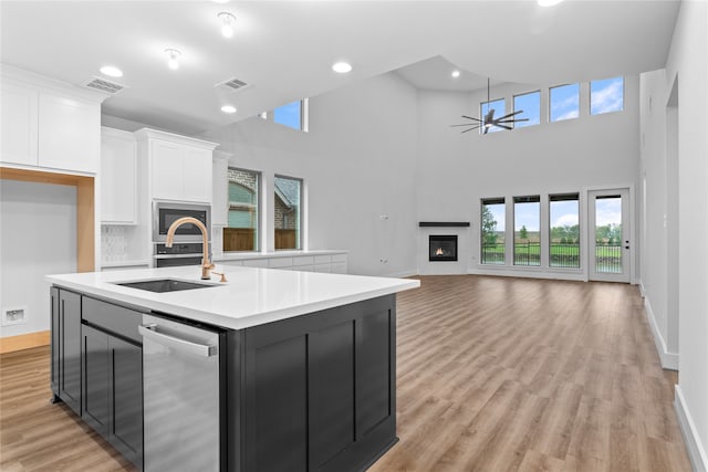 kitchen featuring white cabinetry, a kitchen island with sink, stainless steel appliances, a towering ceiling, and sink