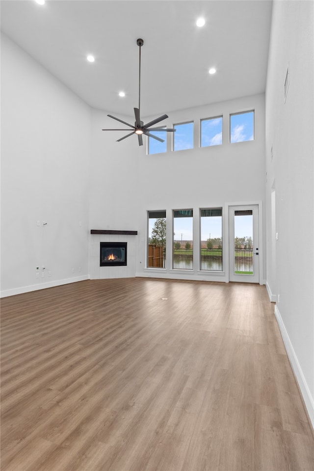 unfurnished living room featuring ceiling fan, a towering ceiling, light hardwood / wood-style flooring, and a fireplace