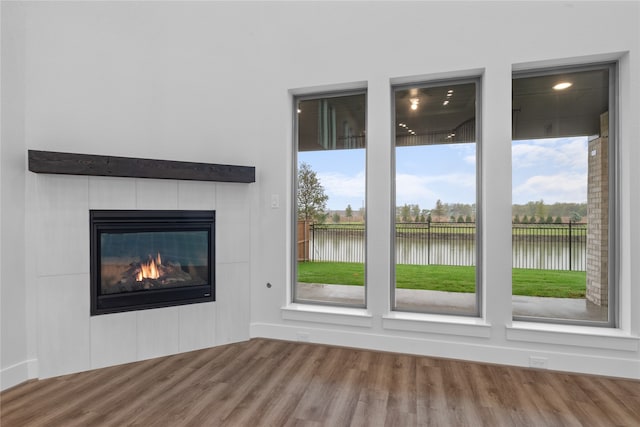 unfurnished living room with a water view, a tiled fireplace, and wood-type flooring