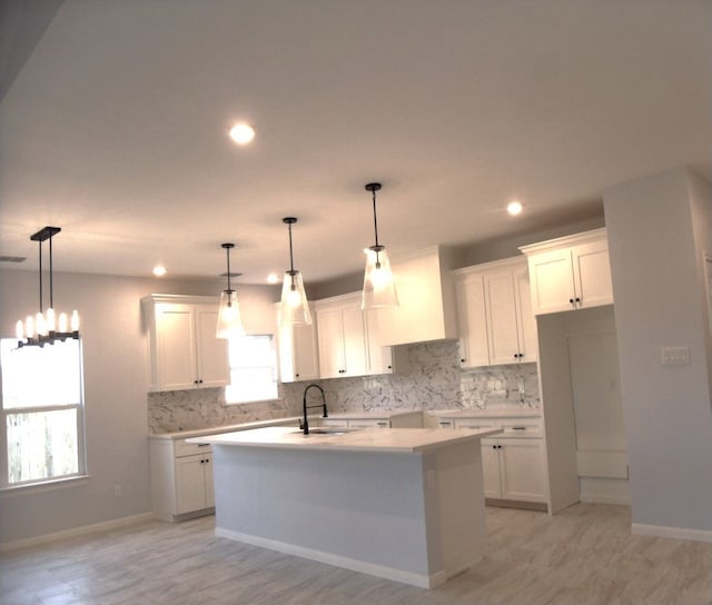 kitchen featuring sink, white cabinets, pendant lighting, and an island with sink