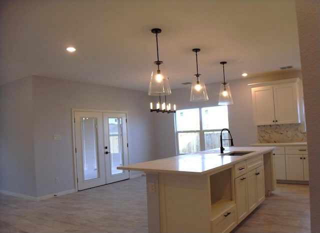 kitchen featuring white cabinets, hanging light fixtures, a center island with sink, light wood-type flooring, and sink