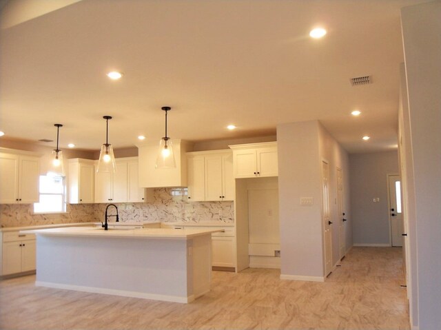 kitchen featuring backsplash, decorative light fixtures, an island with sink, and white cabinets