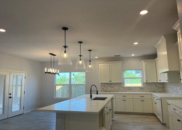 kitchen with tasteful backsplash, hanging light fixtures, an island with sink, light wood-type flooring, and sink