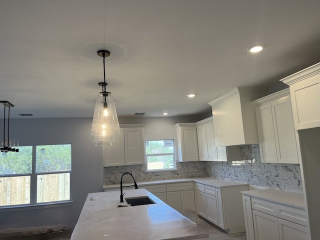 kitchen with hanging light fixtures, sink, white cabinets, light hardwood / wood-style floors, and tasteful backsplash