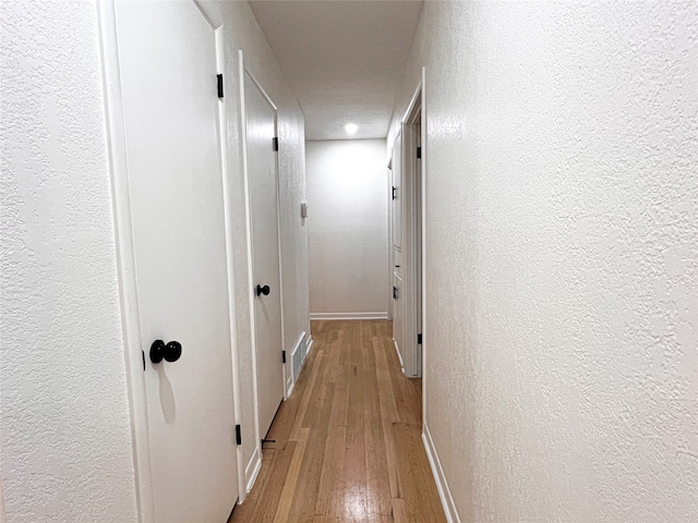 corridor with light hardwood / wood-style floors and a textured ceiling