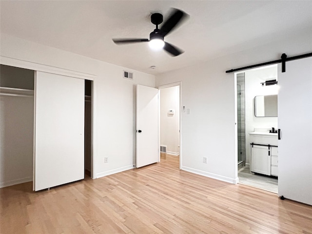 unfurnished bedroom with connected bathroom, a closet, light hardwood / wood-style flooring, a barn door, and ceiling fan