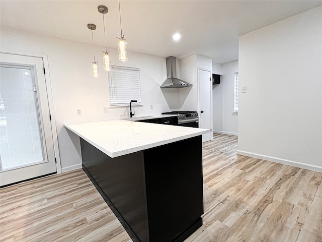 kitchen with wall chimney exhaust hood, hanging light fixtures, kitchen peninsula, light wood-type flooring, and stainless steel range with gas cooktop