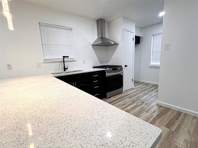 kitchen with kitchen peninsula, stainless steel range with gas stovetop, light hardwood / wood-style floors, wall chimney exhaust hood, and sink