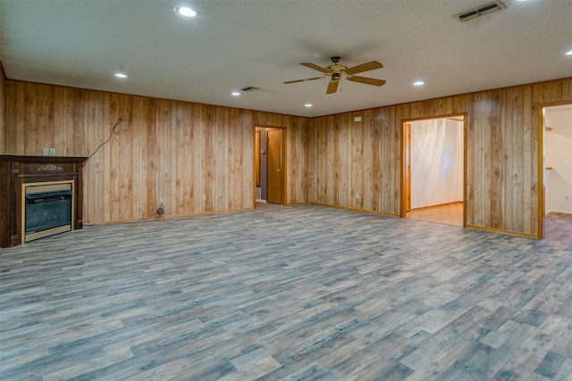 unfurnished living room featuring hardwood / wood-style flooring, ceiling fan, a textured ceiling, and wood walls