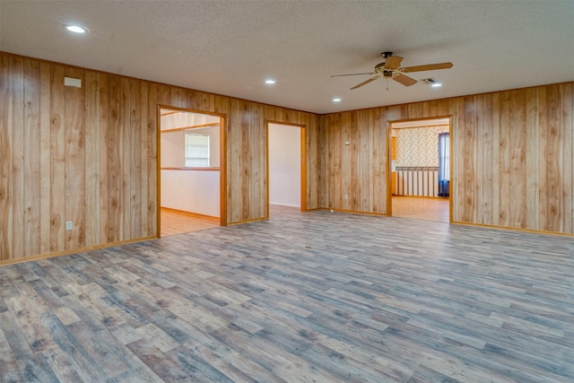 unfurnished room featuring ceiling fan, wood-type flooring, a textured ceiling, and wood walls