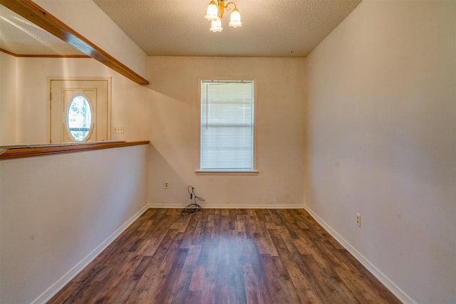 empty room featuring an inviting chandelier, dark hardwood / wood-style floors, and a textured ceiling