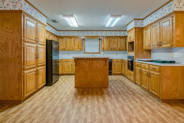 kitchen featuring light hardwood / wood-style flooring, a textured ceiling, a kitchen island, and black appliances