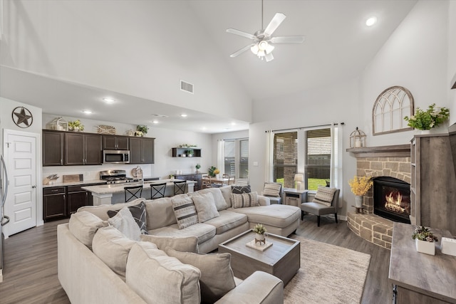 living room with a stone fireplace, high vaulted ceiling, dark wood-type flooring, and ceiling fan