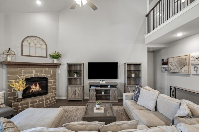 living room featuring a towering ceiling, dark wood-type flooring, a fireplace, and ceiling fan