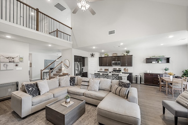 living room with ceiling fan, a towering ceiling, and wood-type flooring