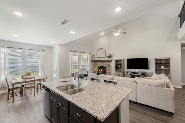 kitchen with a center island with sink, dark hardwood / wood-style flooring, dishwasher, a stone fireplace, and sink